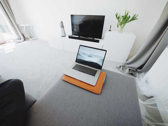 A couch with an opened laptop near the edge. The background shows a tv on a white desk.