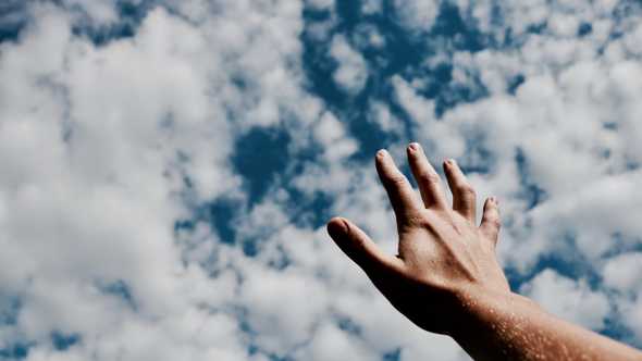 A hand reaching towards a cloudy sky.