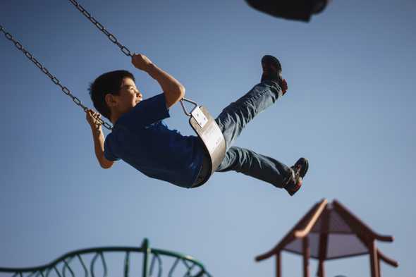 A boy having fun on a swing. The background shows a bright sky and some other kids' playground equipment