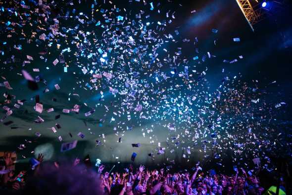 Lots of confetti on a dark background above a partying crowd.